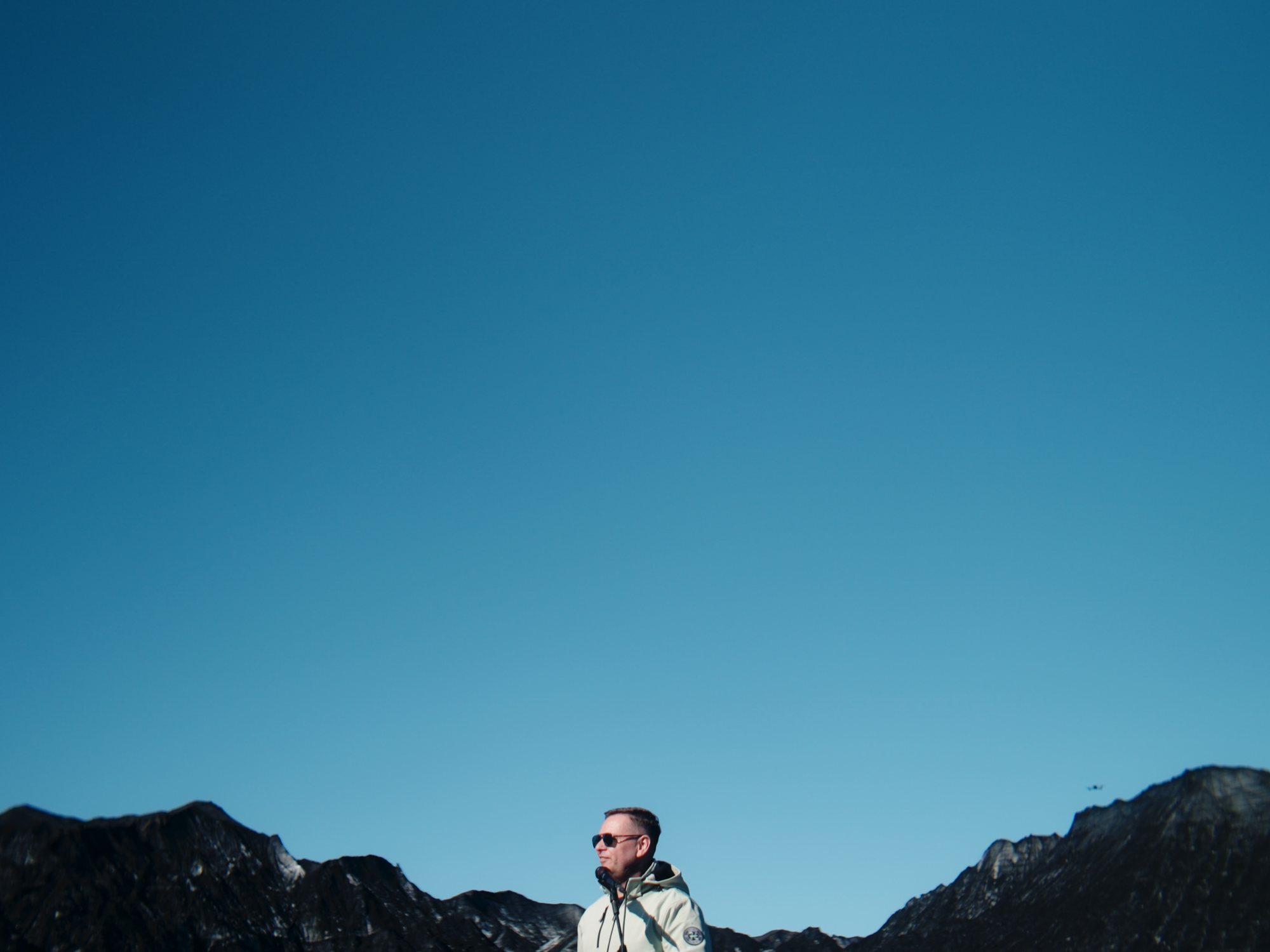 A man standing small on a ridge under a deep blue Icelandic sky
