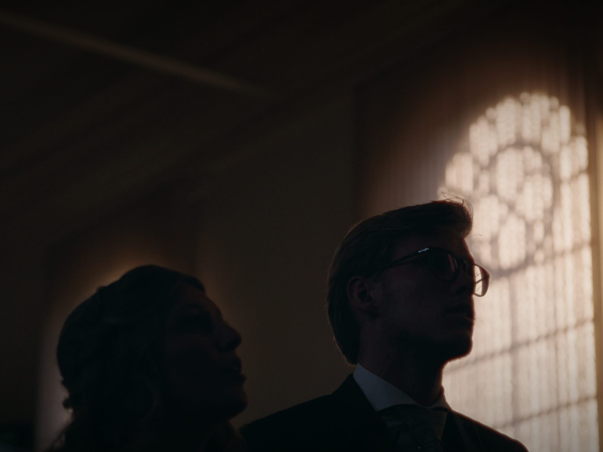 Two silhouettes in a church, lit by a rose window